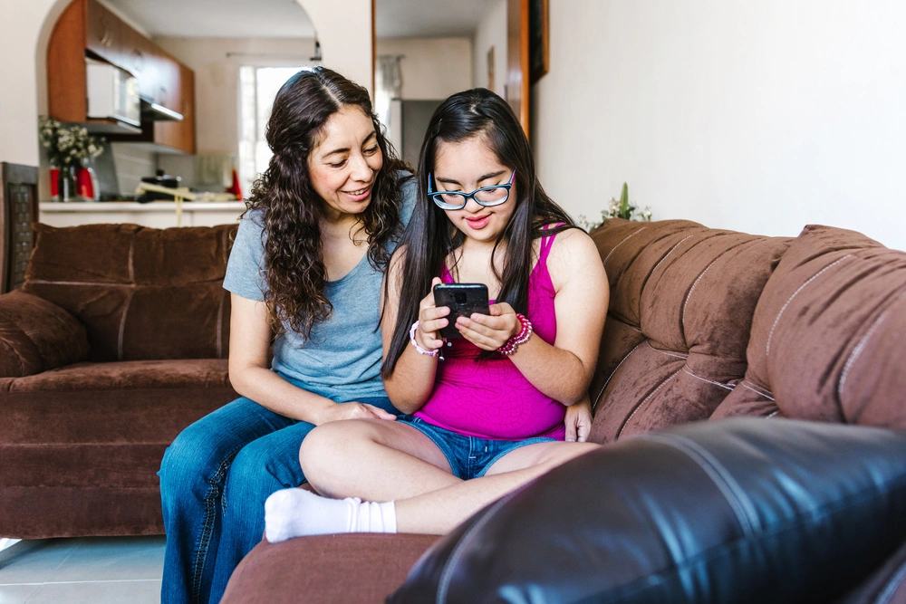 mother with disabled daughter with down syndrome disability sitting on sofa