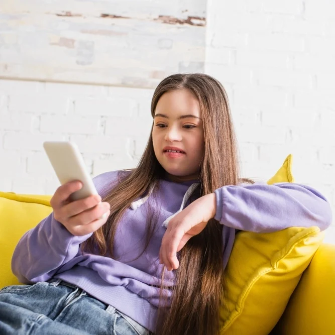 Disabled women with down syndrome disability sitting on sofa and using phone